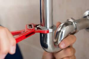 Plumber using a wrench to tighten a nut on a pipe under the sink